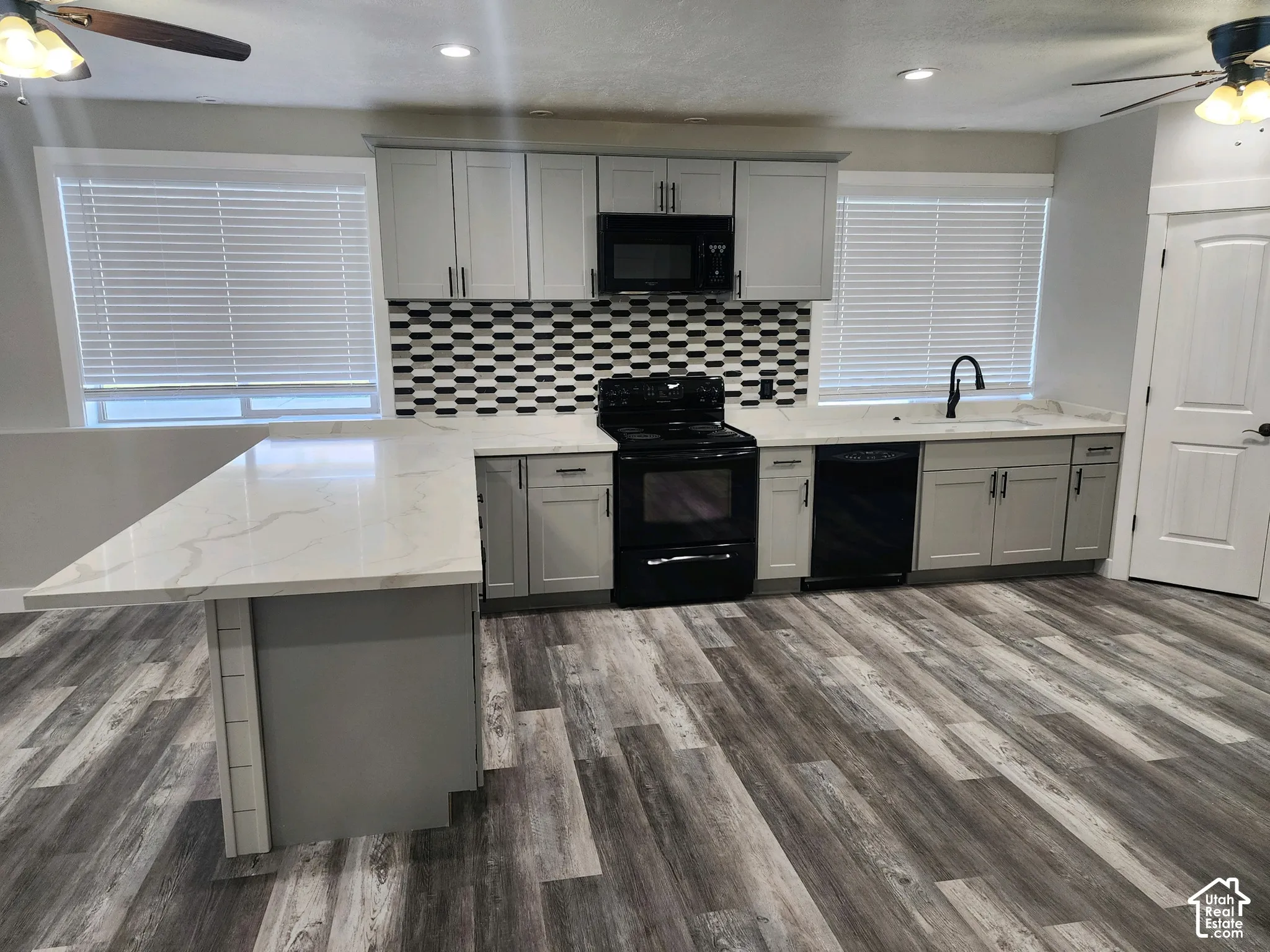 Kitchen featuring gray shaker-style cabinetry, white countertops with integrated veining, a patterned geometric tile backsplash, black appliances, and wood-finish flooring