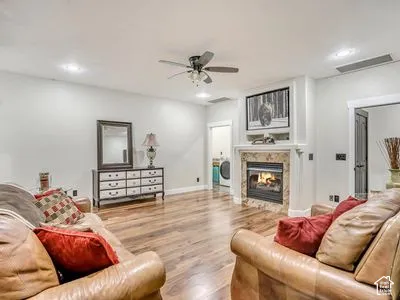 Fireplace with natural stone surround and integrated built-in cabinetry, wood-finish flooring, recessed lighting, and a ceiling fan