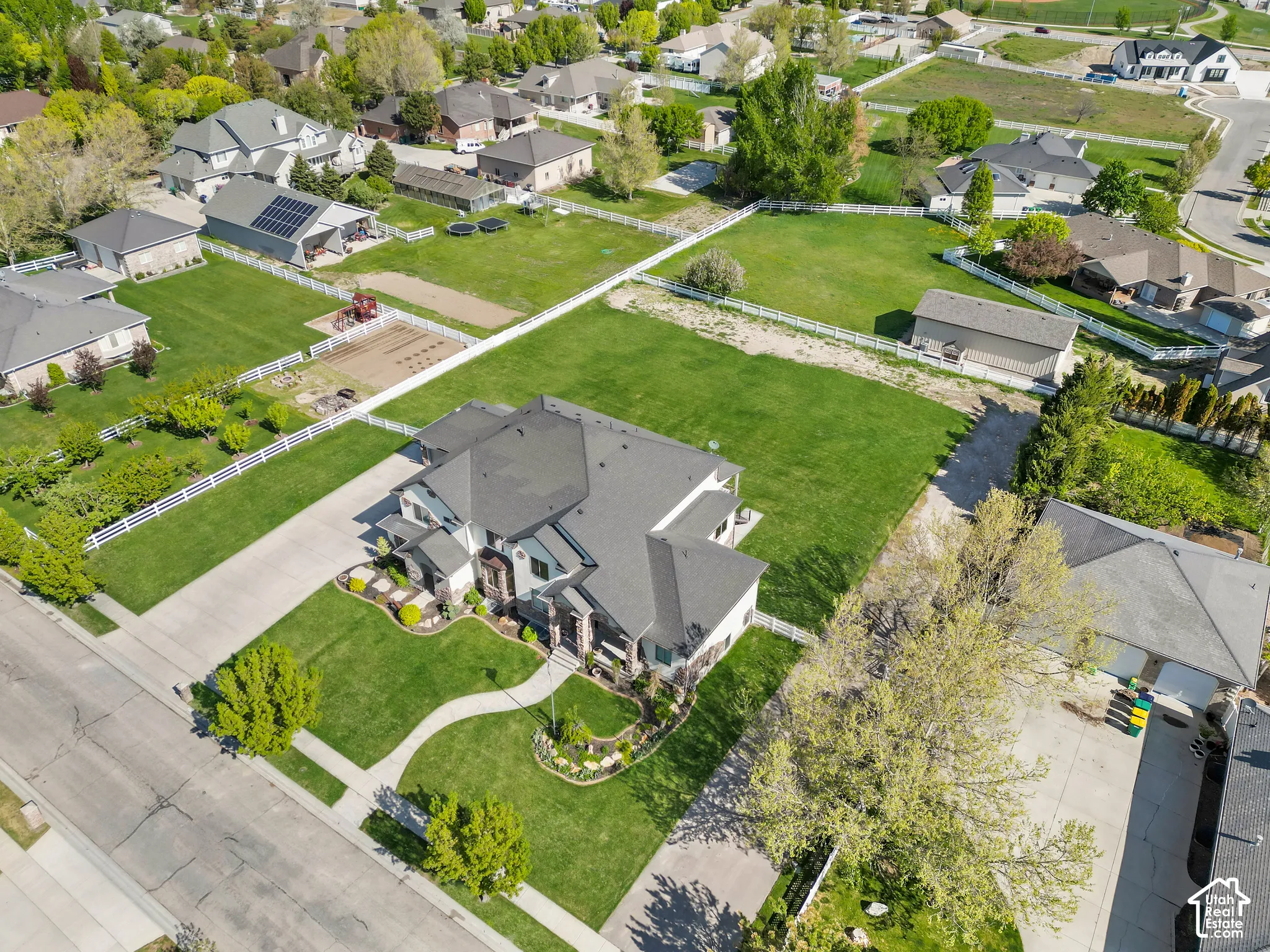 Aerial perspective featuring an expansive lot, manicured lawn, multi-gabled roofline, concrete driveway, and white perimeter fencing