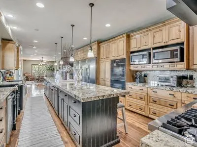 Kitchen featuring custom wood cabinetry, an oversized central island with a contrasting dark finish, natural stone countertops, stainless steel built-in appliances, and wood-finish flooring