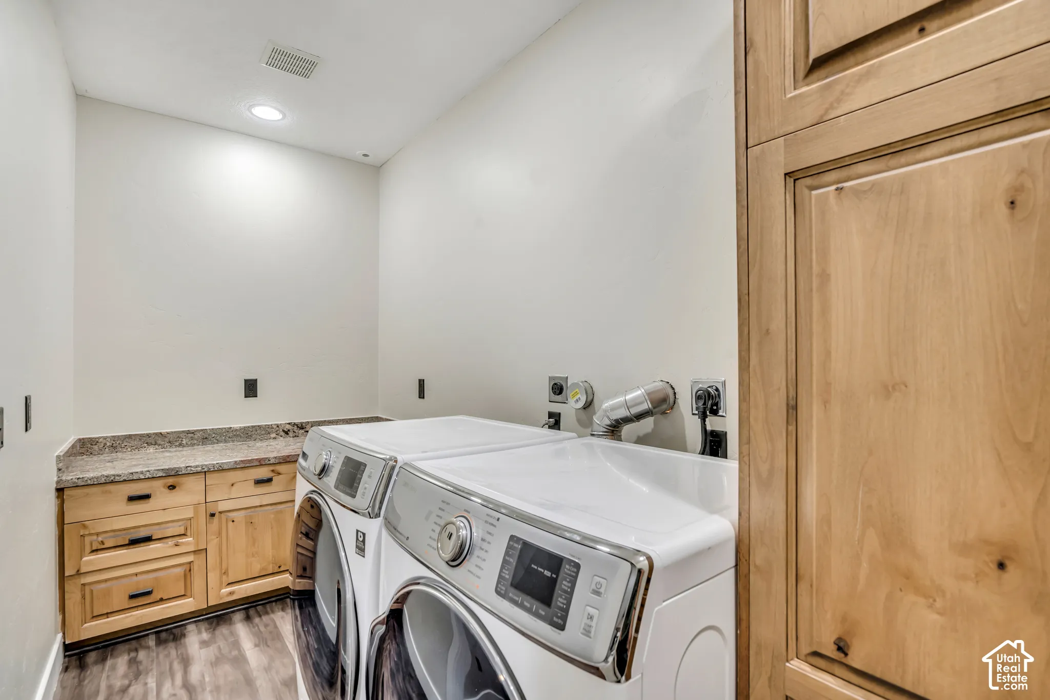 Laundry area featuring custom light wood cabinetry, stone-surface countertop, floor-to-ceiling storage pantry, and wood-finish flooring