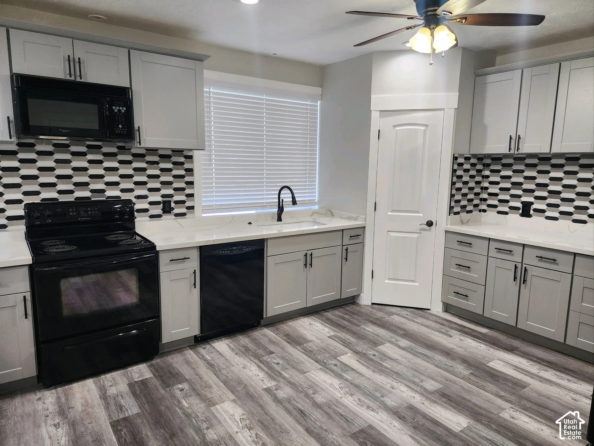 Kitchen featuring shaker-style cabinetry, patterned tile backsplash, wood-finish flooring, solid surface countertops, and black appliance suite