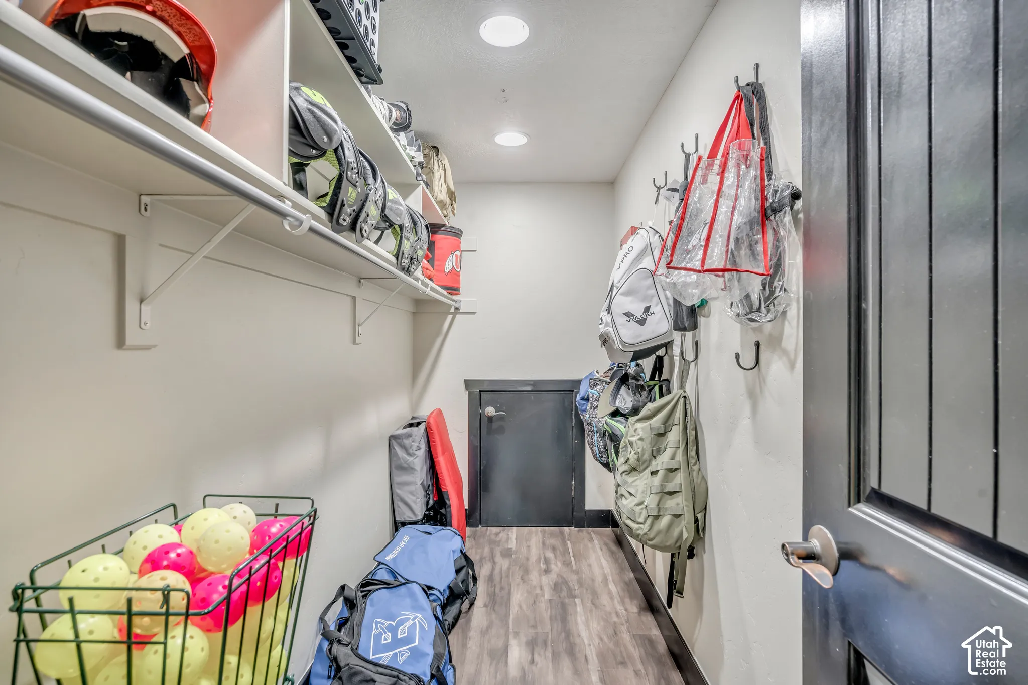 Storage room featuring wood-finish flooring, white built-in shelving, mounted wall hooks, and recessed ceiling lighting