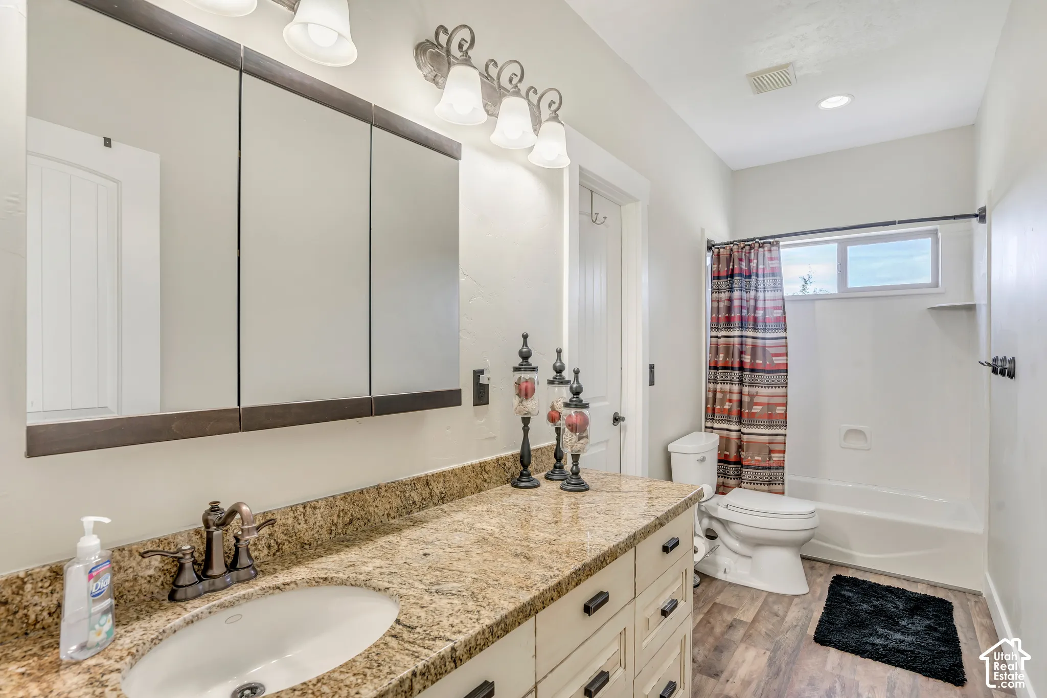 Bathroom vanity featuring a stone-look countertop with an undermount sink, multi-panel wall-mounted medicine cabinet, oil-rubbed bronze fixtures, wood-finish flooring, and a tub-shower combination