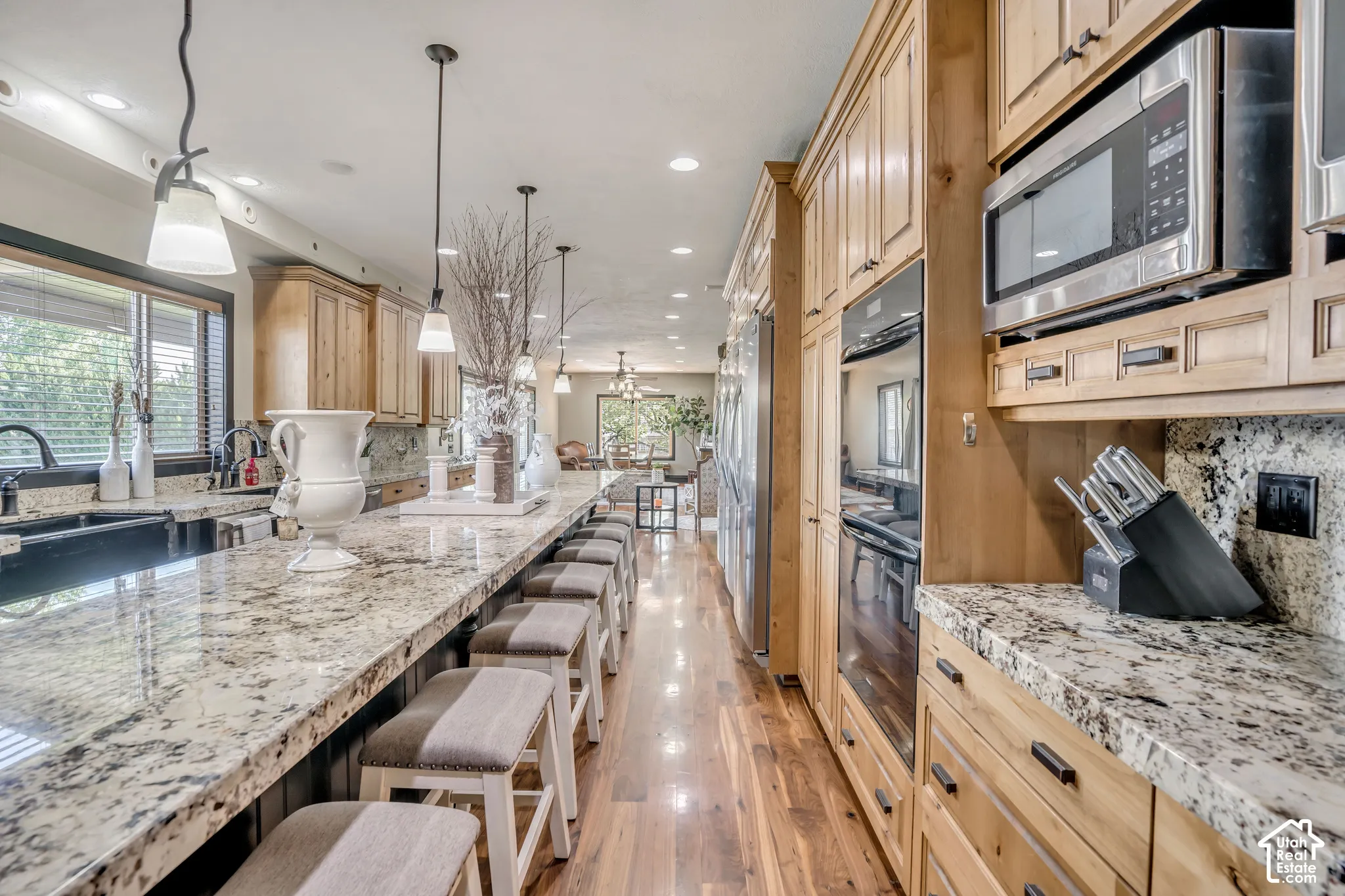 Kitchen featuring custom wood cabinetry, expansive stone countertops, stainless steel wall-mounted oven and microwave, and wood-finish flooring