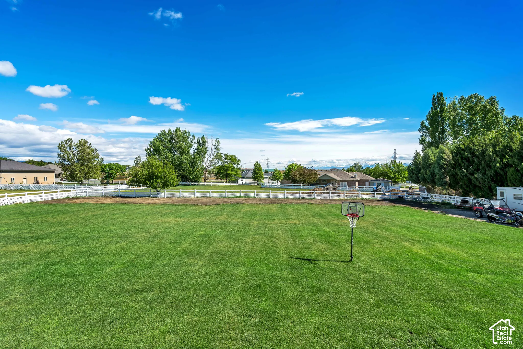Expansive open lawn enclosed by white vinyl perimeter fencing and mature trees