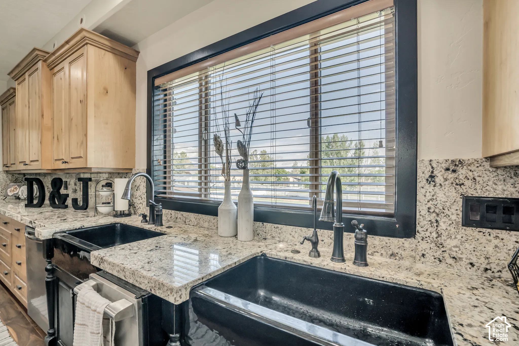 Kitchen featuring speckled stone countertops, dual black apron-front sinks, natural wood cabinetry, and a high-arch matte black faucet
