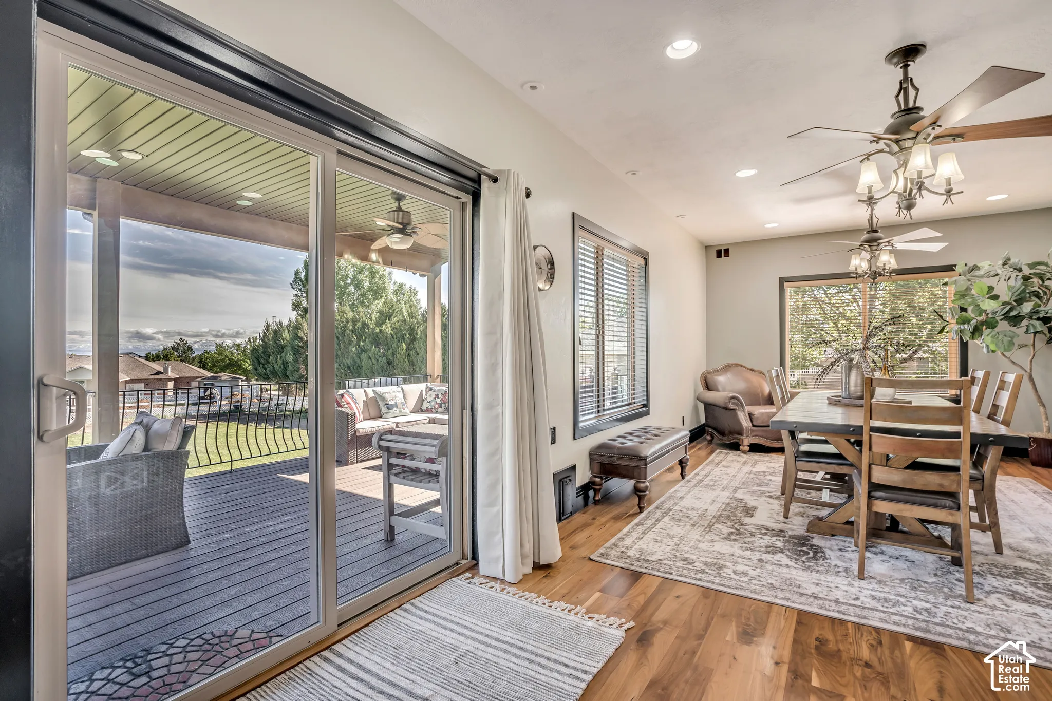 Dining area featuring wood-finish flooring, recessed lighting, and dual ceiling fans, with glass sliding doors leading to a covered outdoor deck with iron railings