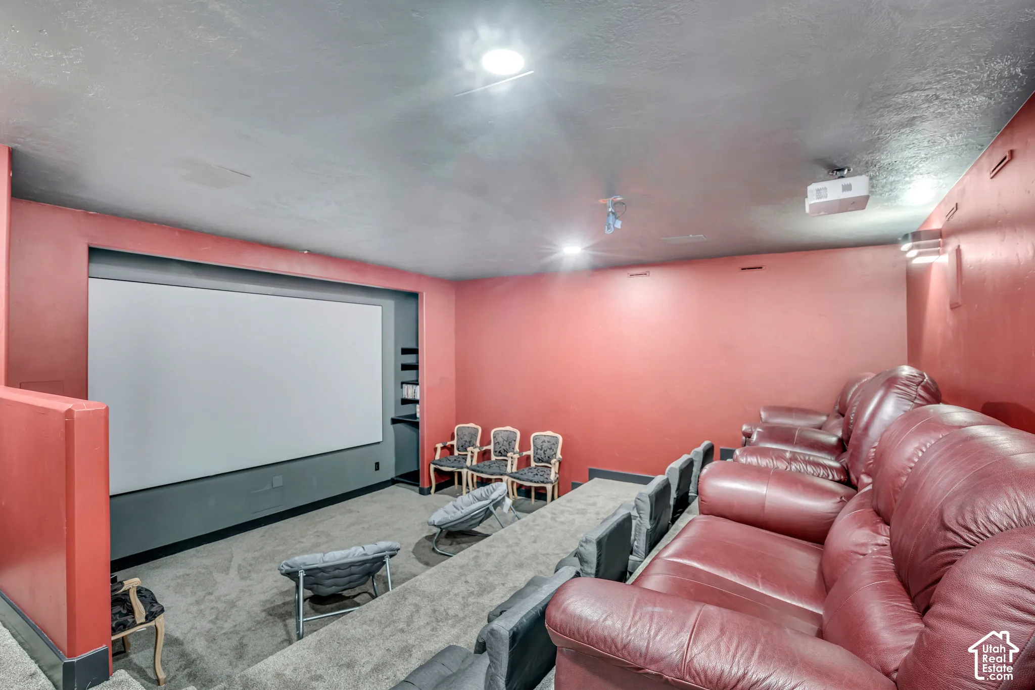 Dedicated media room featuring a built-in projector screen, recessed ceiling lighting, wall-mounted projection equipment, multi-level tiered flooring, and integrated wall shelving