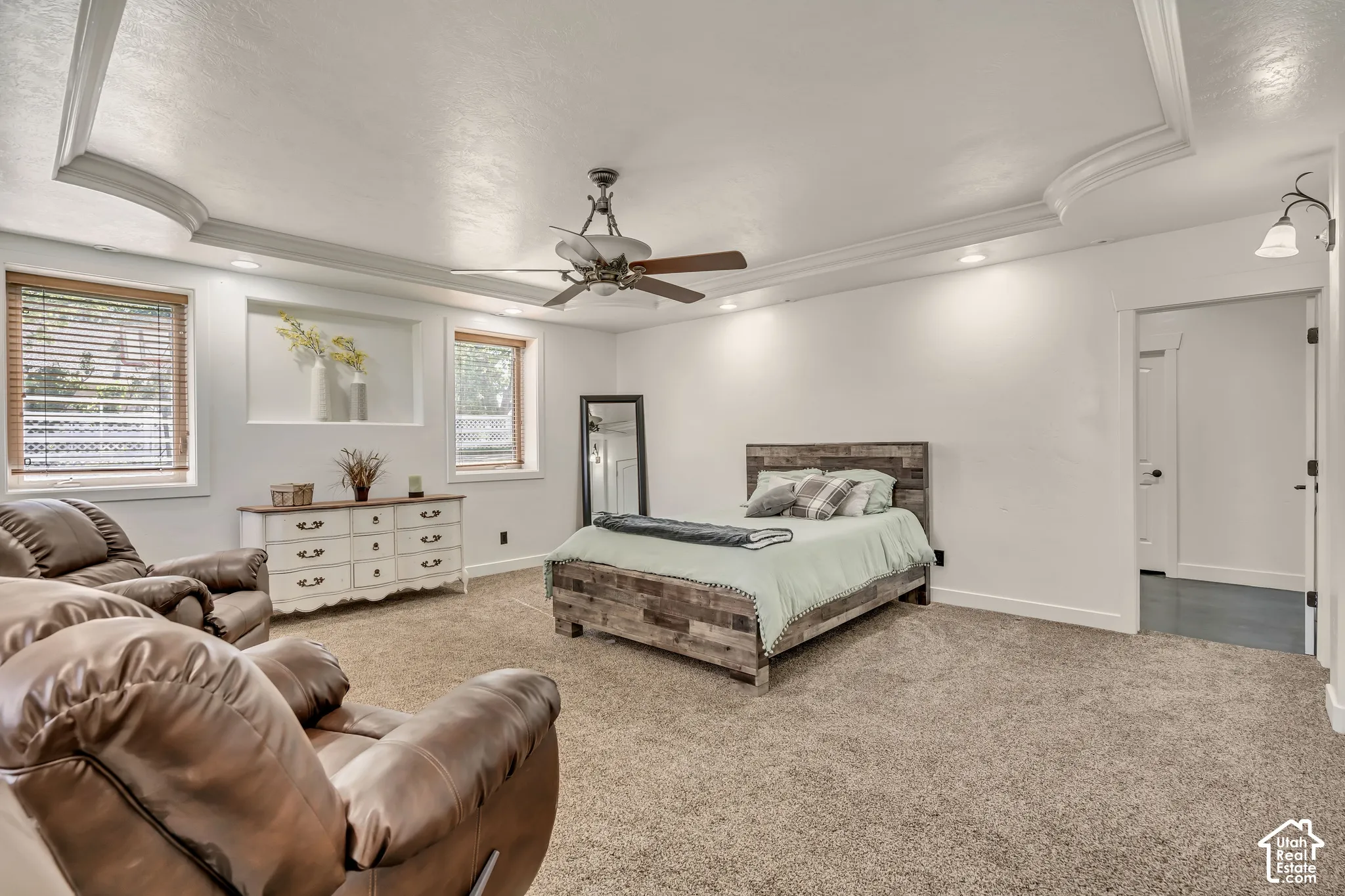 Spacious room featuring a recessed tray ceiling, neutral wall-to-wall carpeting, recessed lighting, a central ceiling fan, and a built-in wall niche