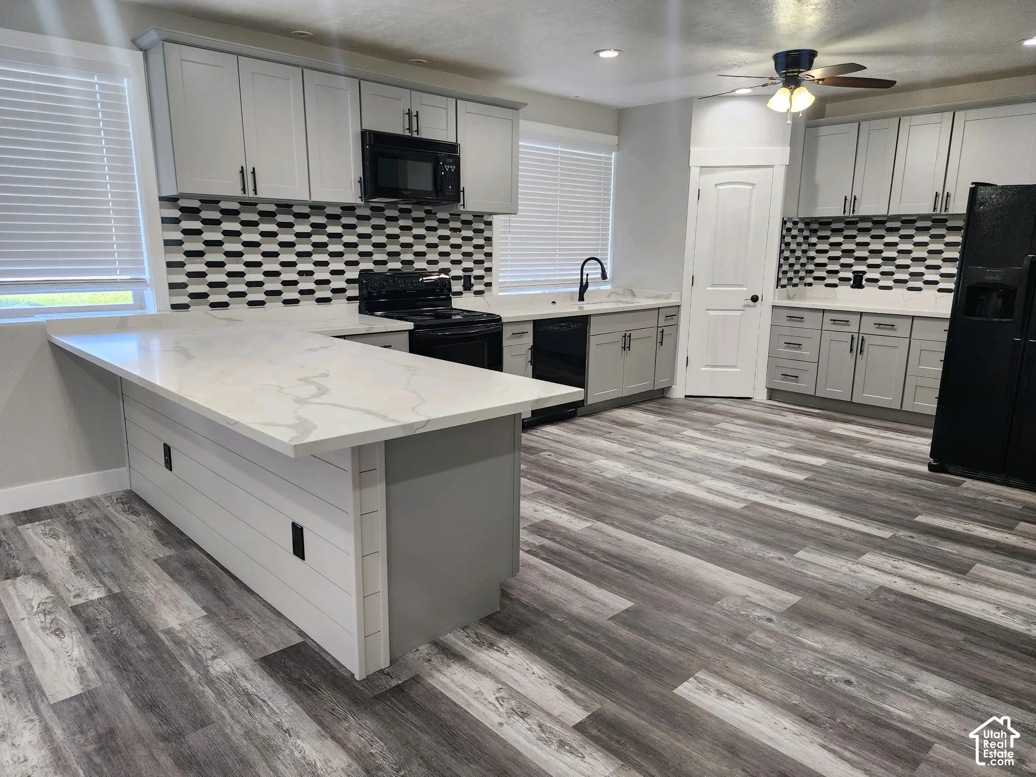 Kitchen featuring light-gray cabinetry, stone-finish countertops, patterned tile backsplash, wood-finish flooring, and a shiplap-accented kitchen island