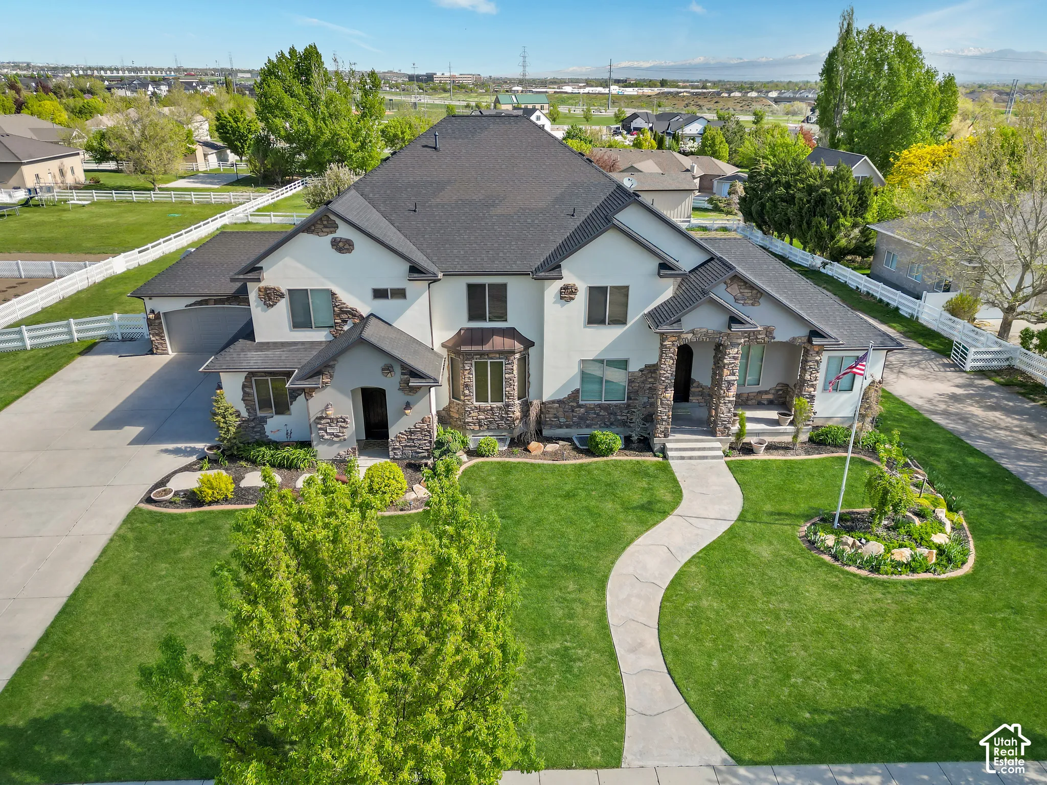 Two-story residence featuring a mixed stucco and stone veneer exterior, an asphalt shingle roof, an attached multi-car garage, and a curated landscape with a concrete walkway