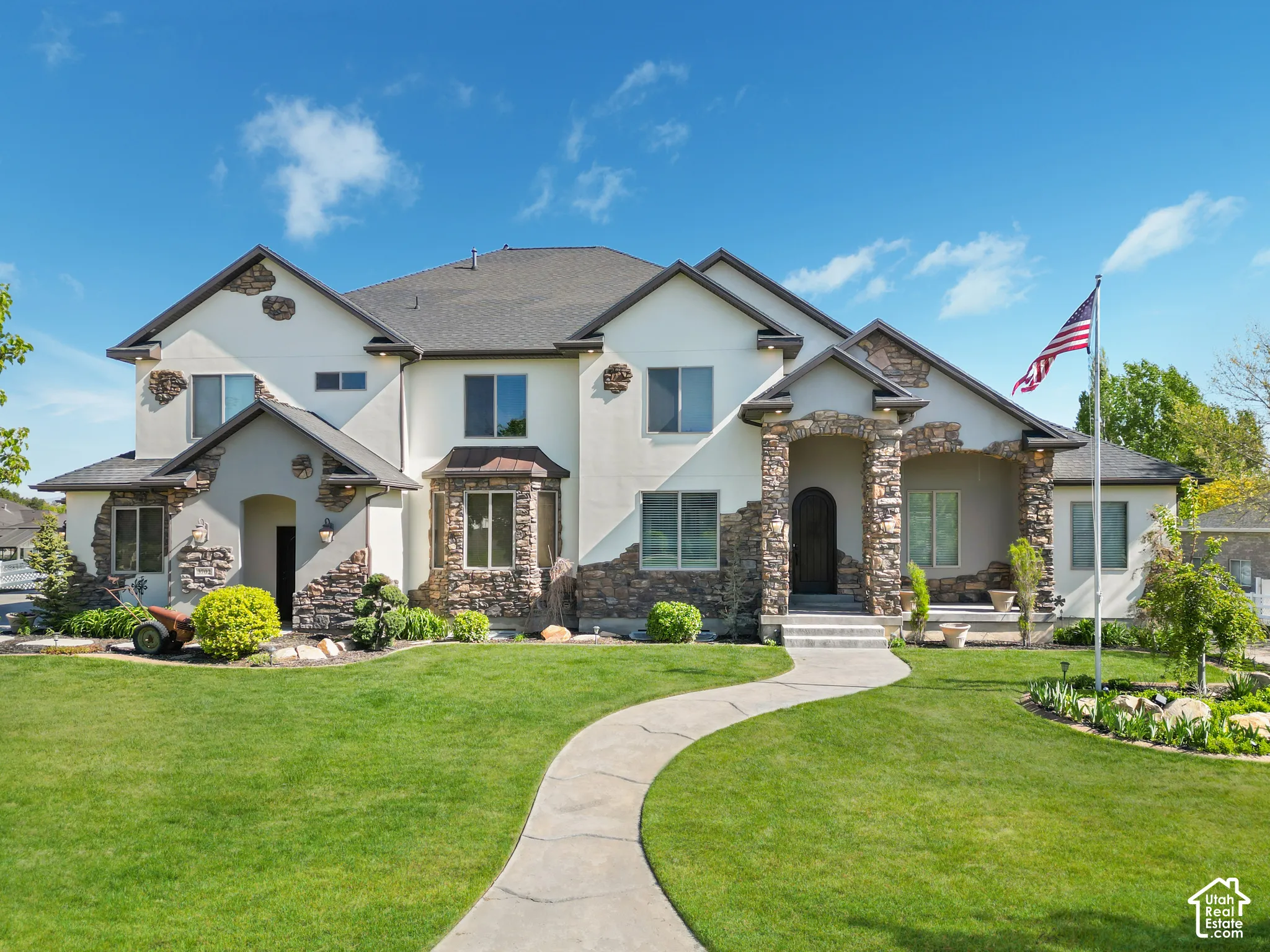 Multi-gabled exterior featuring stucco siding, stone veneer accents, architectural roof shingles, and a curved concrete walkway