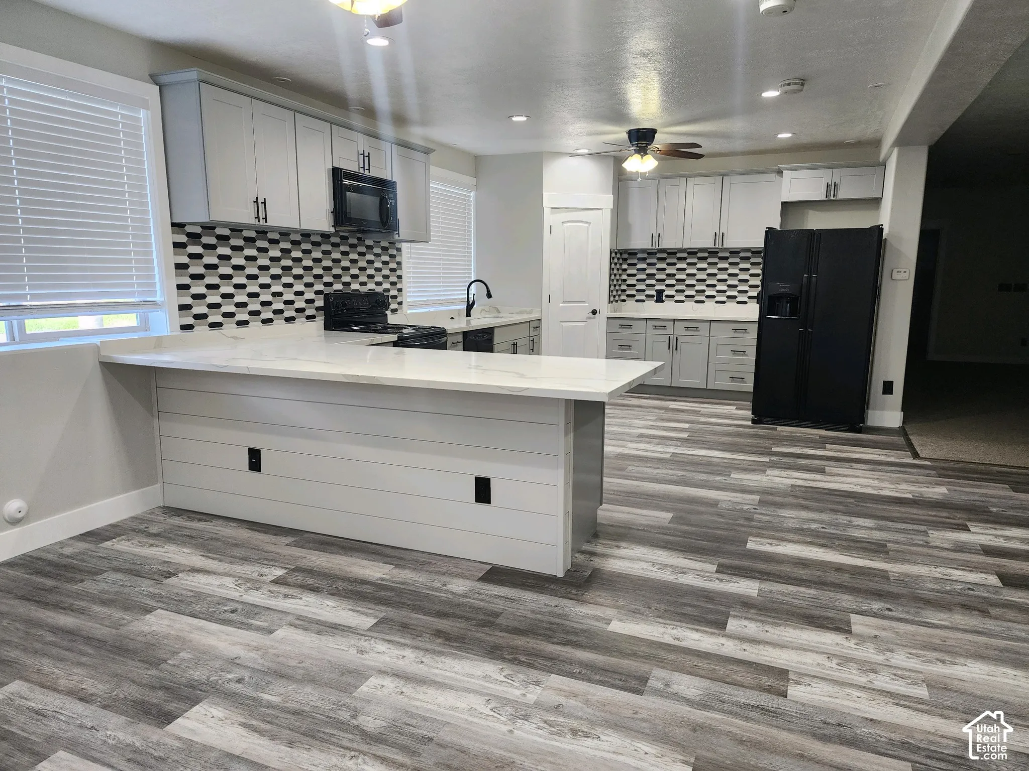 Kitchen featuring light-toned cabinetry, a stone-finish countertop, shiplap detailing on the peninsula, wood-finish flooring, and a patterned tile backsplash