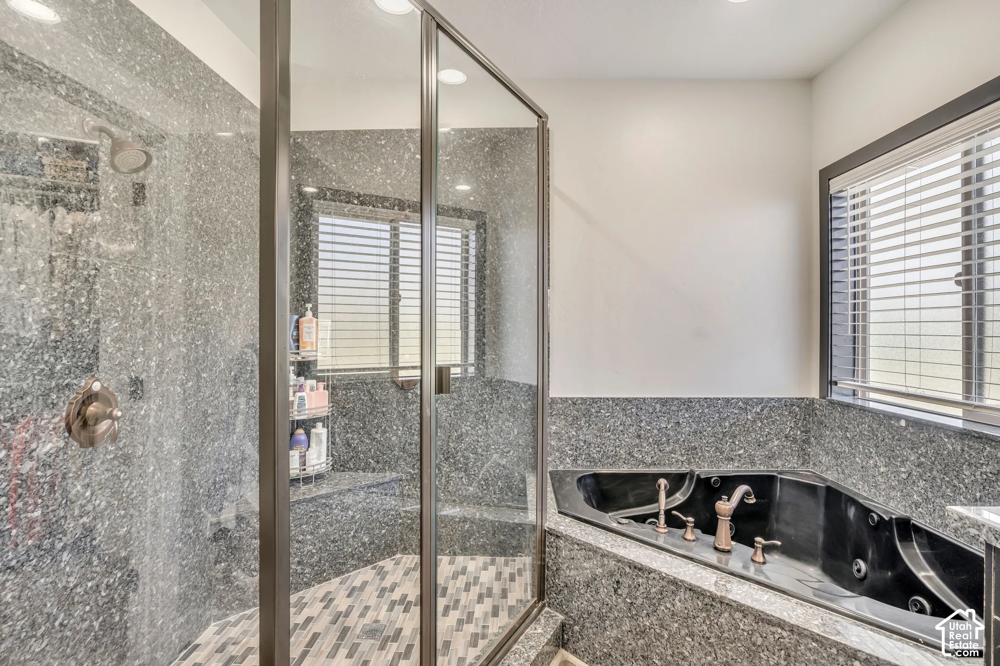 Walk-in shower featuring glass enclosure, stone-finish surround, and patterned tile flooring, accompanied by a corner jetted tub with stone-finish deck and metallic hardware