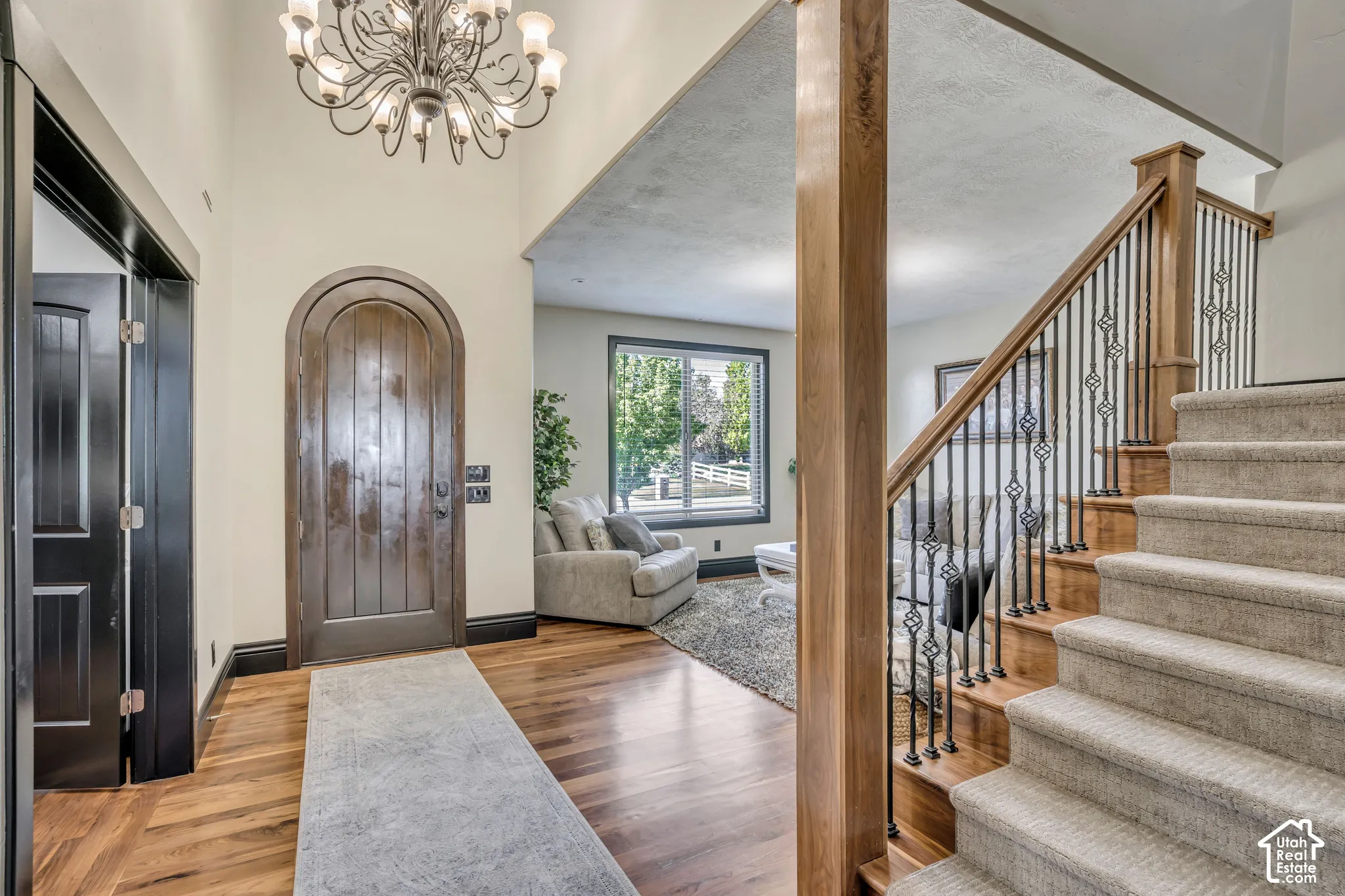 Foyer featuring wood-finish flooring, an arched wood entry door, a multi-tiered chandelier, and a staircase with wood railing and wrought iron balusters