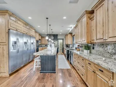 Kitchen featuring custom wood cabinetry, natural stone countertops, a large center island with dark finish cabinetry, wood-finish flooring, and stainless steel refrigeration