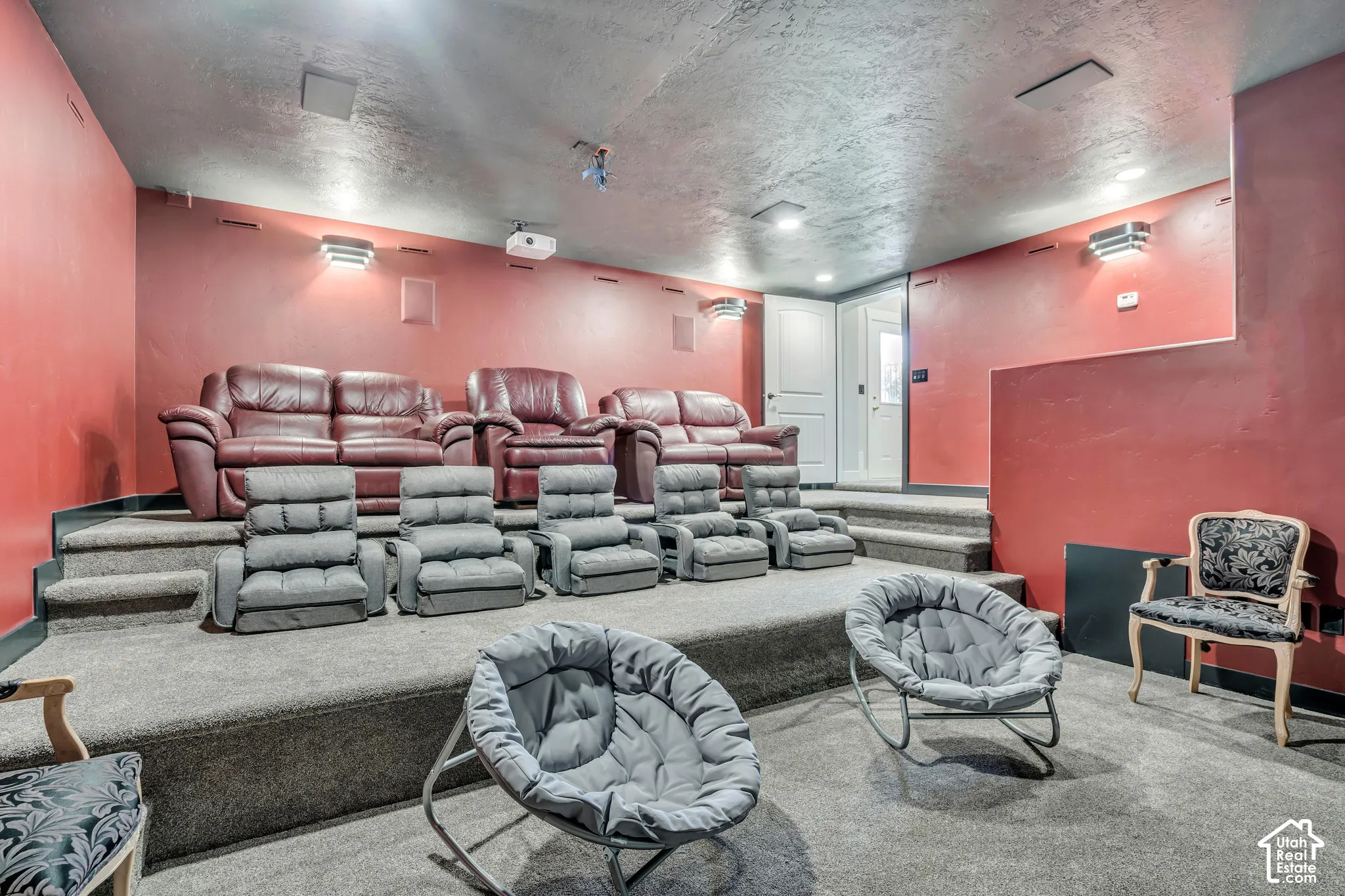 Multi-level media room featuring carpeted tiered seating platforms, wall-mounted lighting fixtures, integrated ceiling speakers, and a mounted projector