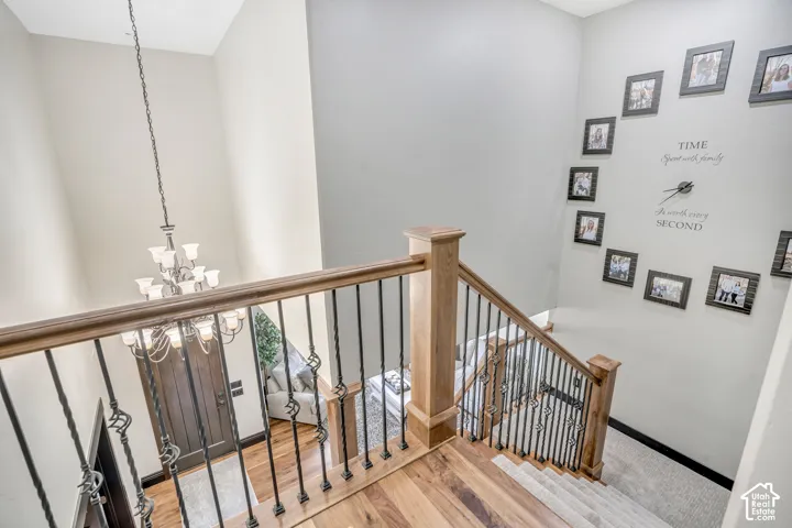 Staircase featuring a wood-finished handrail, decorative metal balusters, and a tiered chandelier