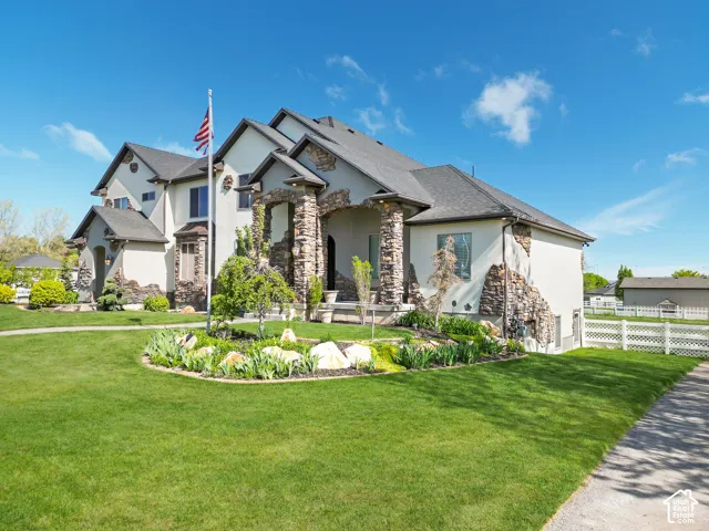 Multi-level exterior featuring light-toned stucco siding, decorative stacked stone accents, covered stone entryway, and a landscaped front garden with rock edging