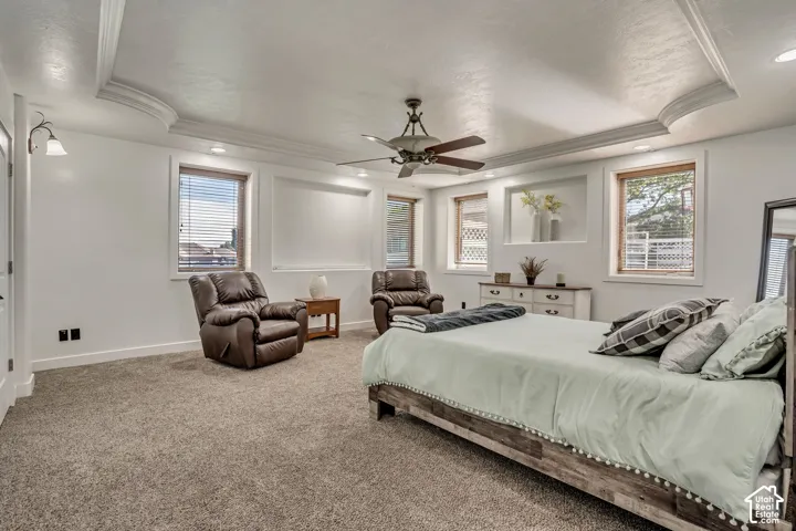 Spacious room featuring a tray ceiling, recessed wall niche, wall-to-wall carpeting, ceiling fan with integrated lighting, and multiple windows