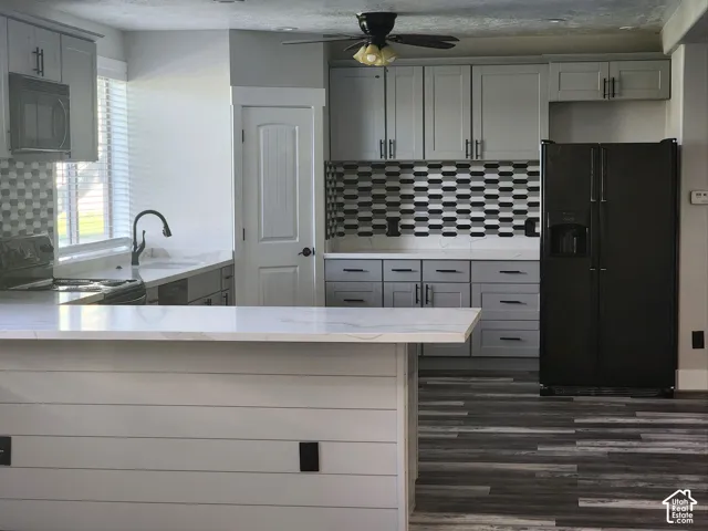 Kitchen featuring gray shaker-style cabinetry, quartz countertops, a patterned tile backsplash, shiplap-accented breakfast bar, and wood-finish flooring
