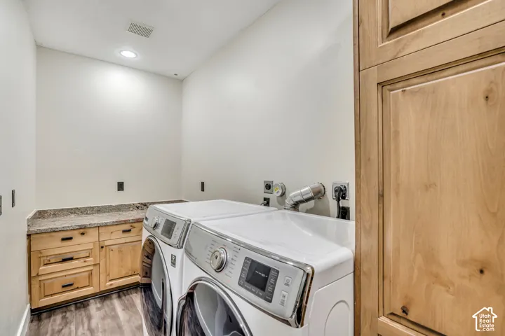 Laundry area featuring custom light wood cabinetry, stone-surface countertop, floor-to-ceiling storage pantry, and wood-finish flooring