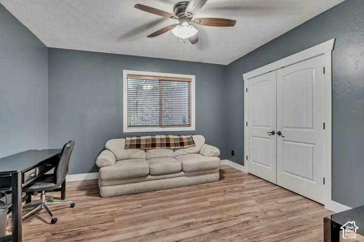 Wood-finish flooring, ceiling fan with integrated lighting, dual-panel closet doors, and window with slat blinds
