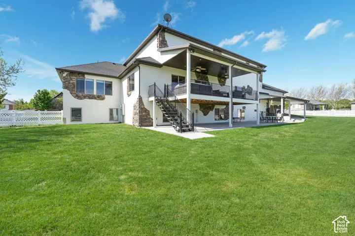 Rear exterior featuring stucco siding with stone accents, a multi-level deck, a covered patio, and expansive lawn space