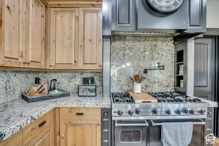 Natural wood-finish cabinetry, stone slab countertops, full-height stone backsplash, professional-grade dual-oven gas range, and wall-mounted pot filler