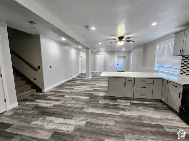 Open-concept kitchen featuring light-toned cabinetry, quartz countertops, wood-finish flooring, recessed lighting, and a multi-paneled staircase with a wood handrail