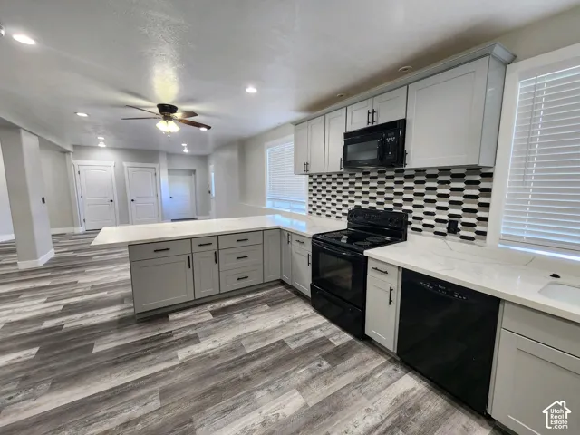 Kitchen featuring gray shaker-style cabinetry, white countertops, patterned tile backsplash, wood-finish flooring, and black appliances