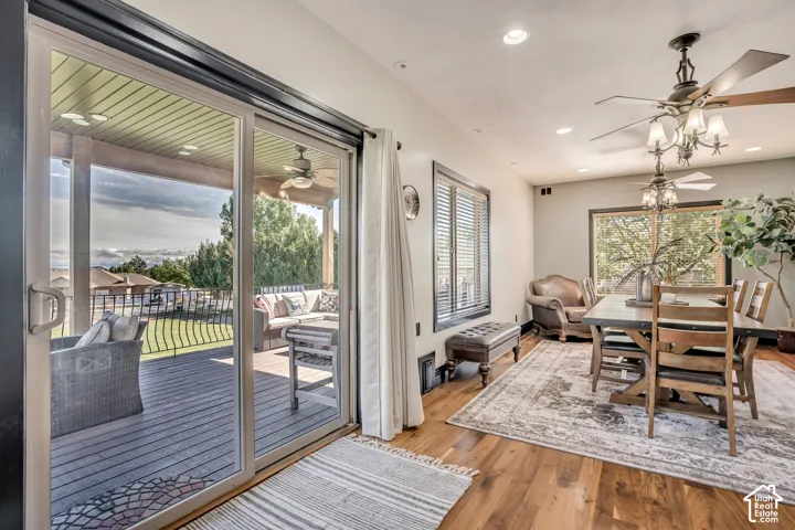 Dining area featuring wood-finish flooring, recessed lighting, and dual ceiling fans, with glass sliding doors leading to a covered outdoor deck with iron railings