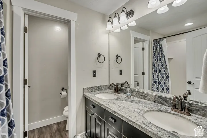 Dual-sink vanity with stone countertop, dark cabinetry, oil-rubbed bronze fixtures, full-width vanity mirror, and three-light sconce