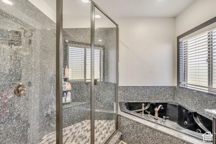 Walk-in shower featuring glass enclosure, stone-finish surround, and patterned tile flooring, accompanied by a corner jetted tub with stone-finish deck and metallic hardware