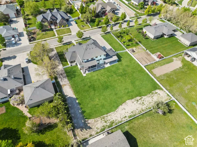 Aerial view of property featuring a multi-pitched roofline, expansive rear lawn, perimeter fencing, and a concrete patio