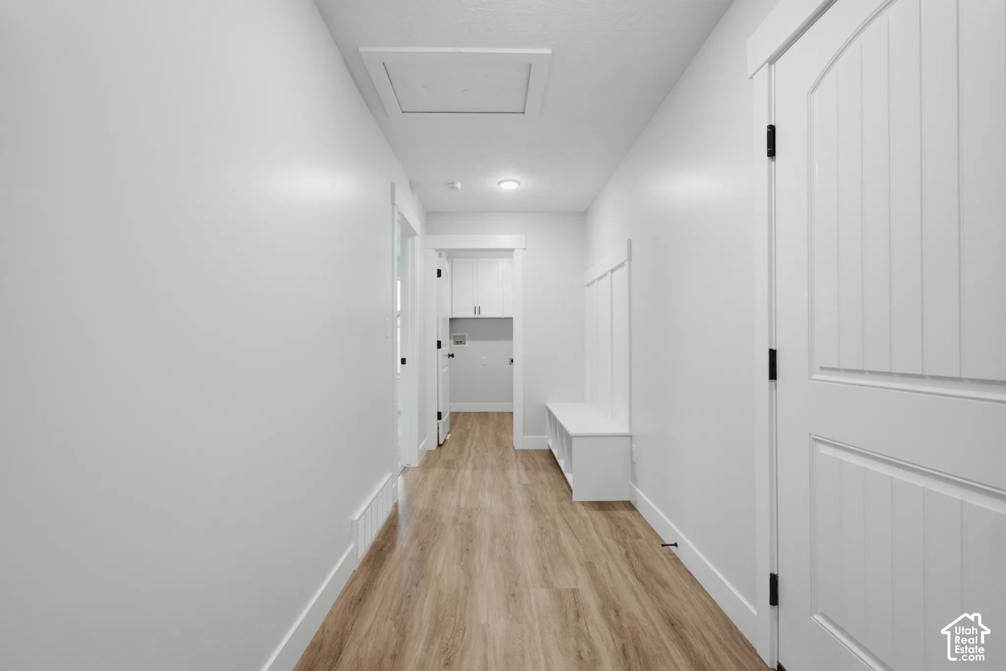 Hallway featuring wood-finish flooring, white paneled doors with black hardware, built-in storage bench with board-and-batten detailing, and recessed ceiling lighting