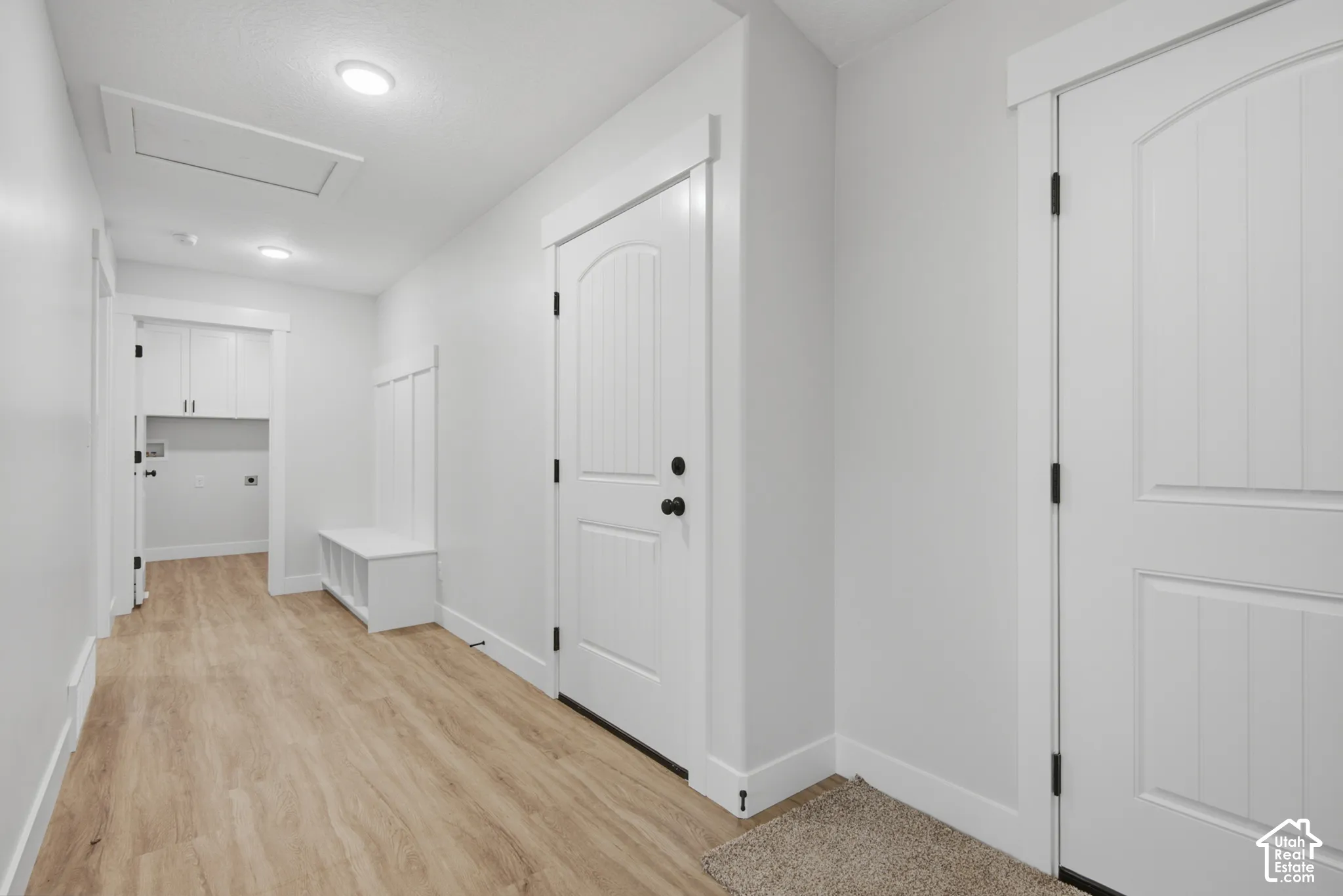 Interior space featuring wood-finish flooring, white paneled doors with matte black hardware, built-in storage bench with beadboard detailing, and recessed ceiling lighting