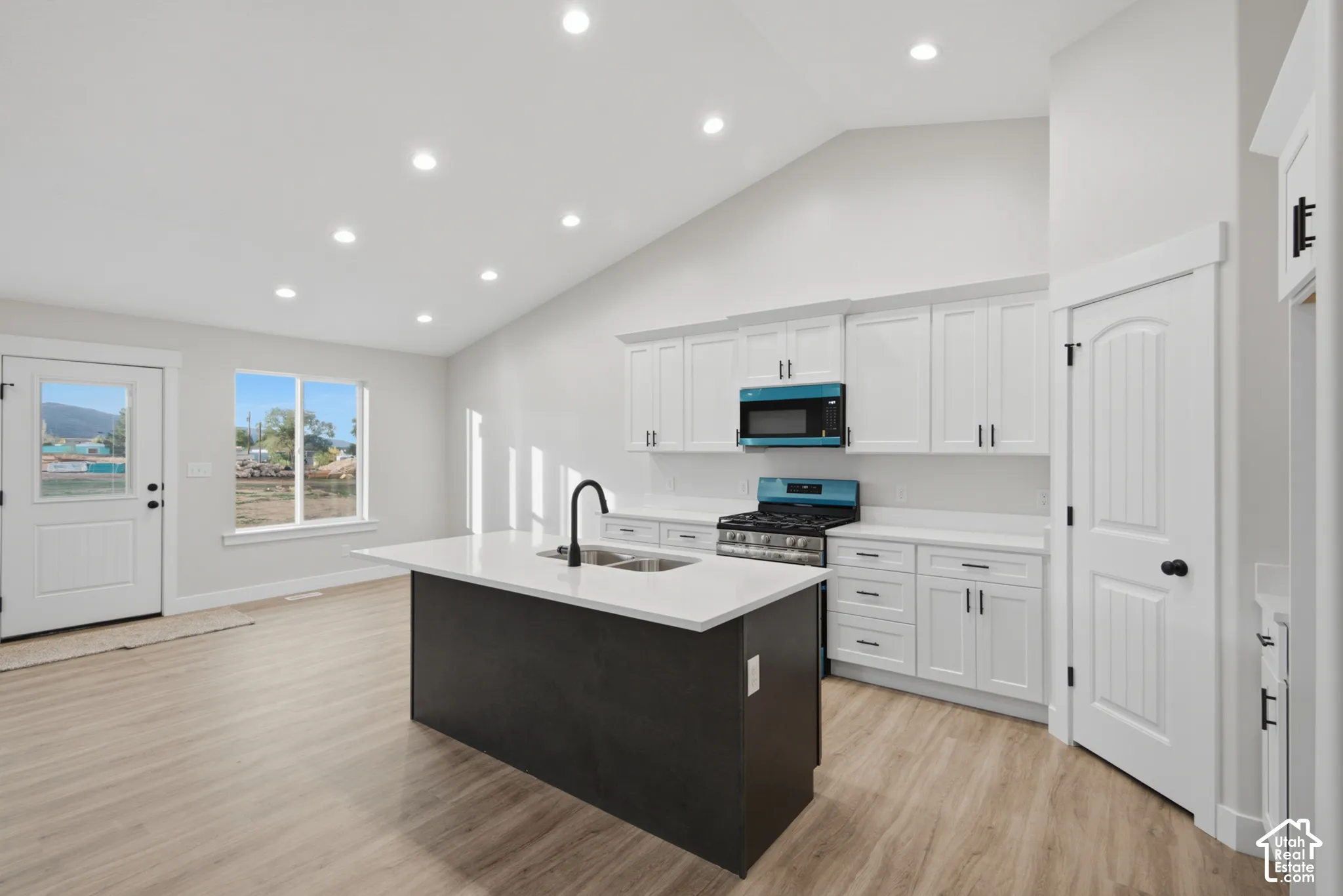 Kitchen featuring white cabinetry, a contrasting dark kitchen island with a stone-surface countertop, wood-finish flooring, recessed lighting, and a vaulted ceiling