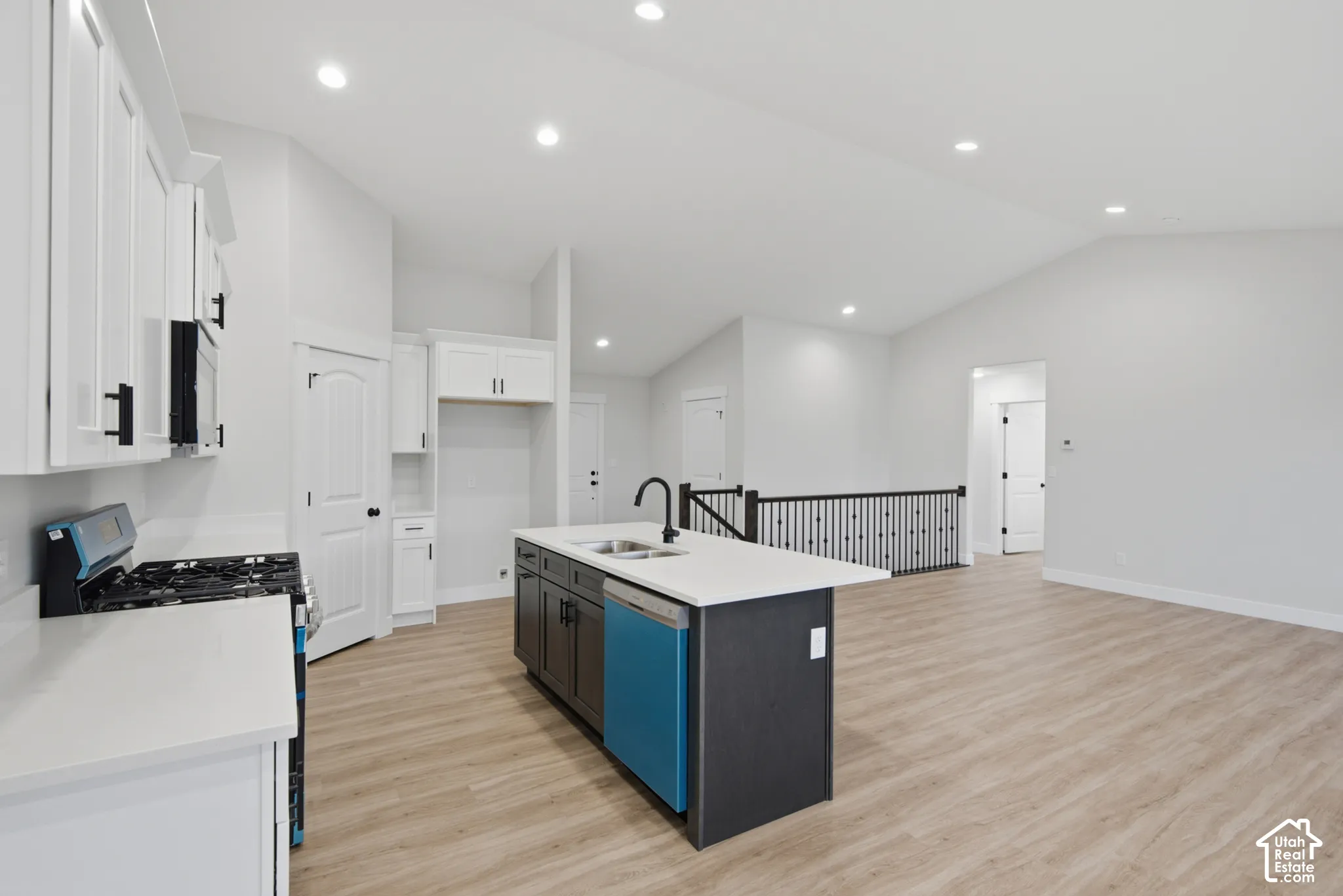 Kitchen featuring white shaker-style cabinetry, quartz countertops, a central island with a matte black faucet, vaulted ceilings, and wood-finish flooring