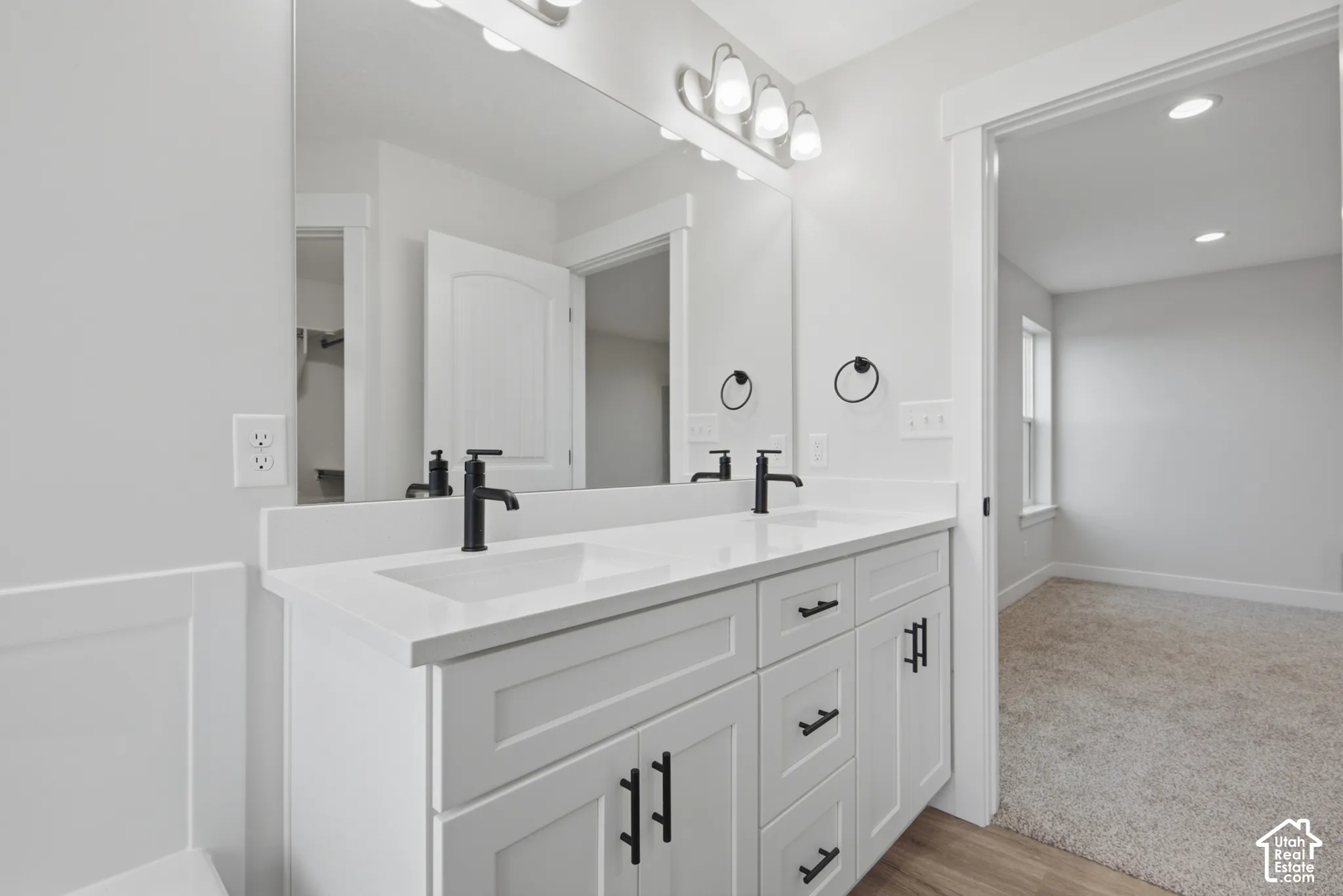 Double vanity featuring white cabinetry, matte black hardware, dual undermount sinks, stone-finish countertops, and a large wall-mounted mirror with multi-bulb lighting