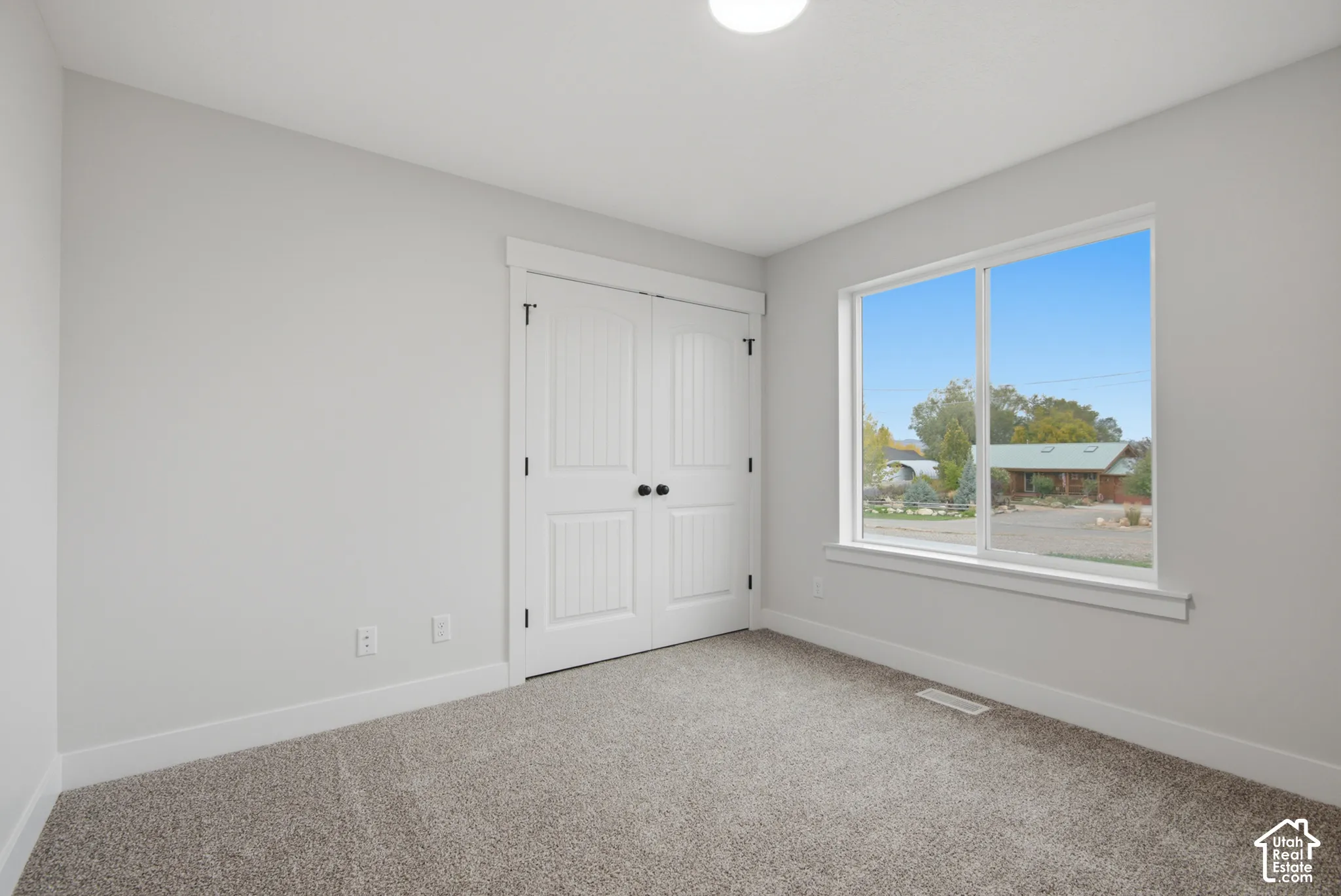 Neutral-toned interior featuring wall-to-wall carpeting, dual-panel closet doors with matte black hardware, and a single-hung window with exterior landscape exposure