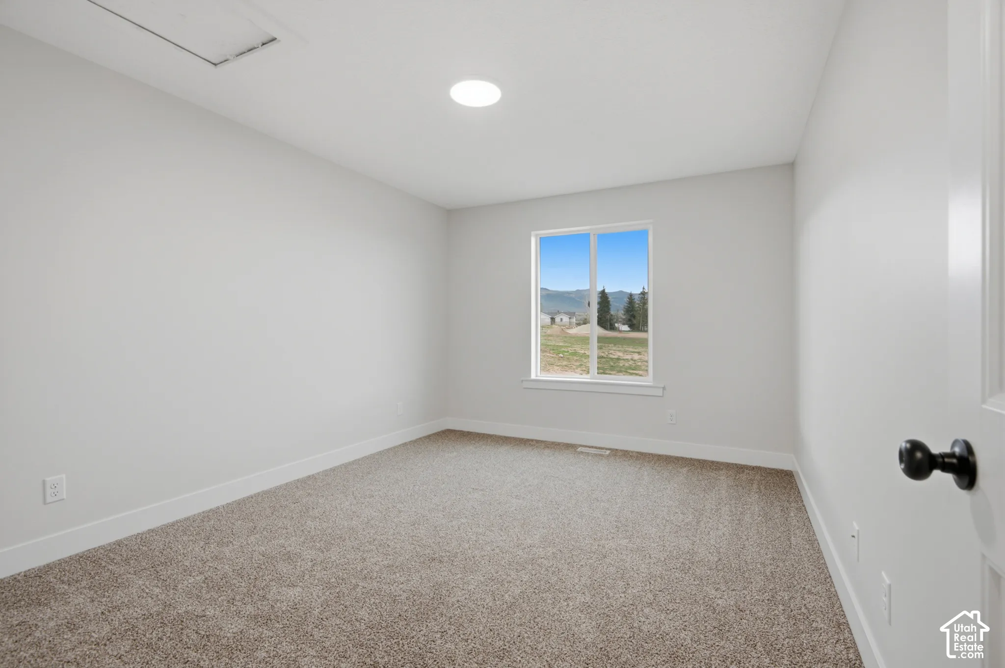 Neutral-toned interior space featuring neutral carpeting, a single-pane window with mountain scenery, a recessed ceiling light, and a matte black door handle