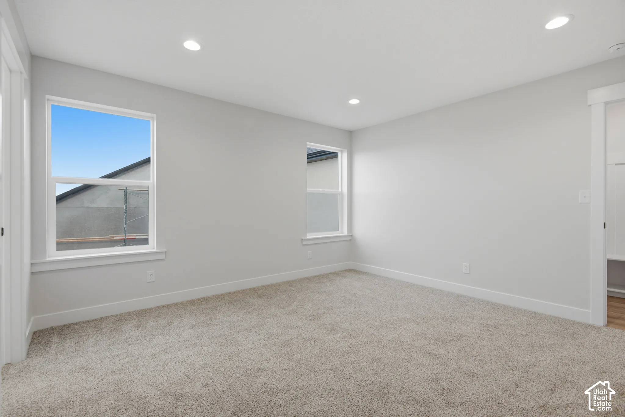 Neutral-toned walls, recessed ceiling lighting, plush wall-to-wall carpeting, and dual windows with crisp white casing