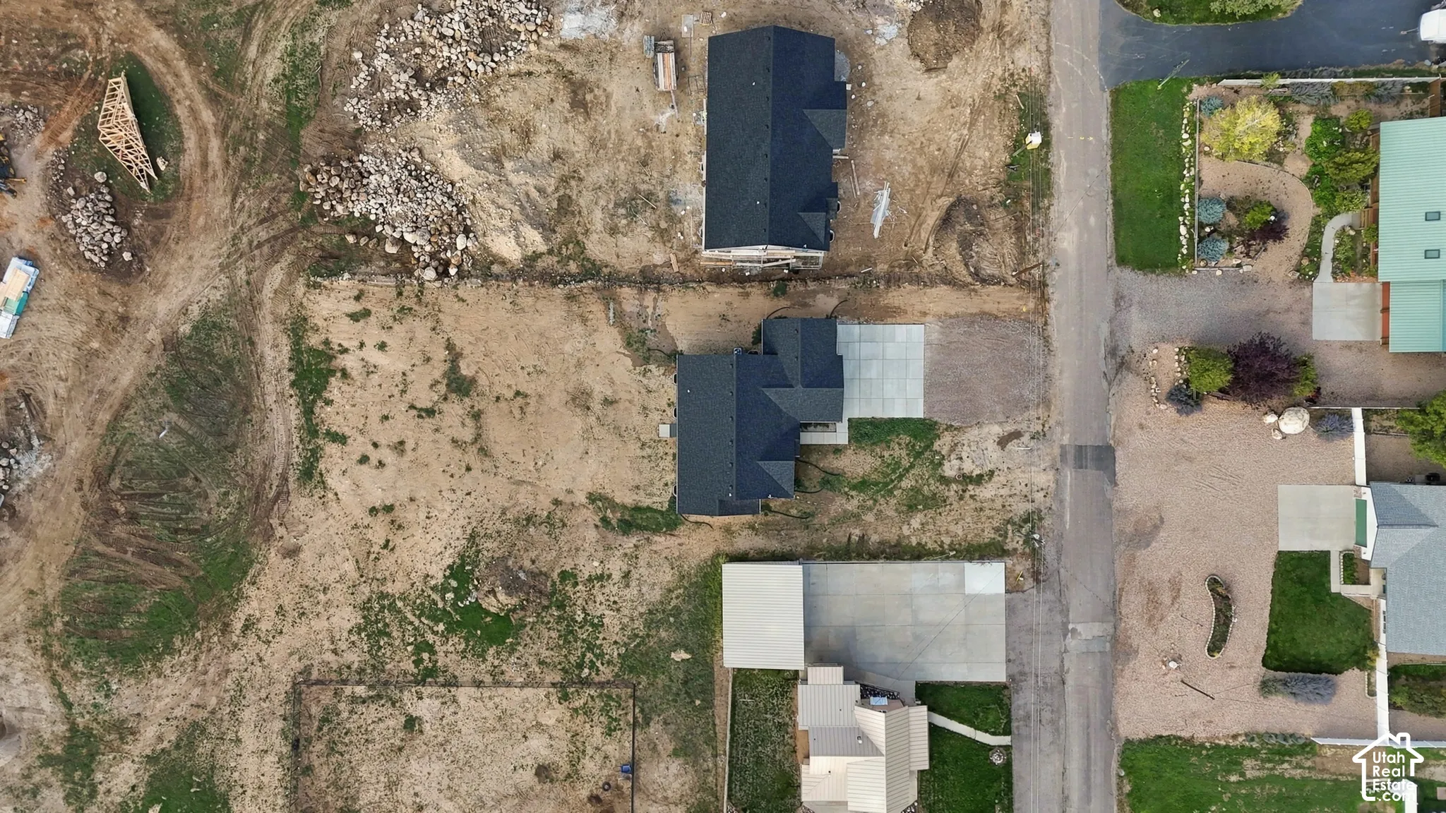 Aerial view of residential property featuring a multi-gabled dark shingle roof, concrete driveway, and cleared lot