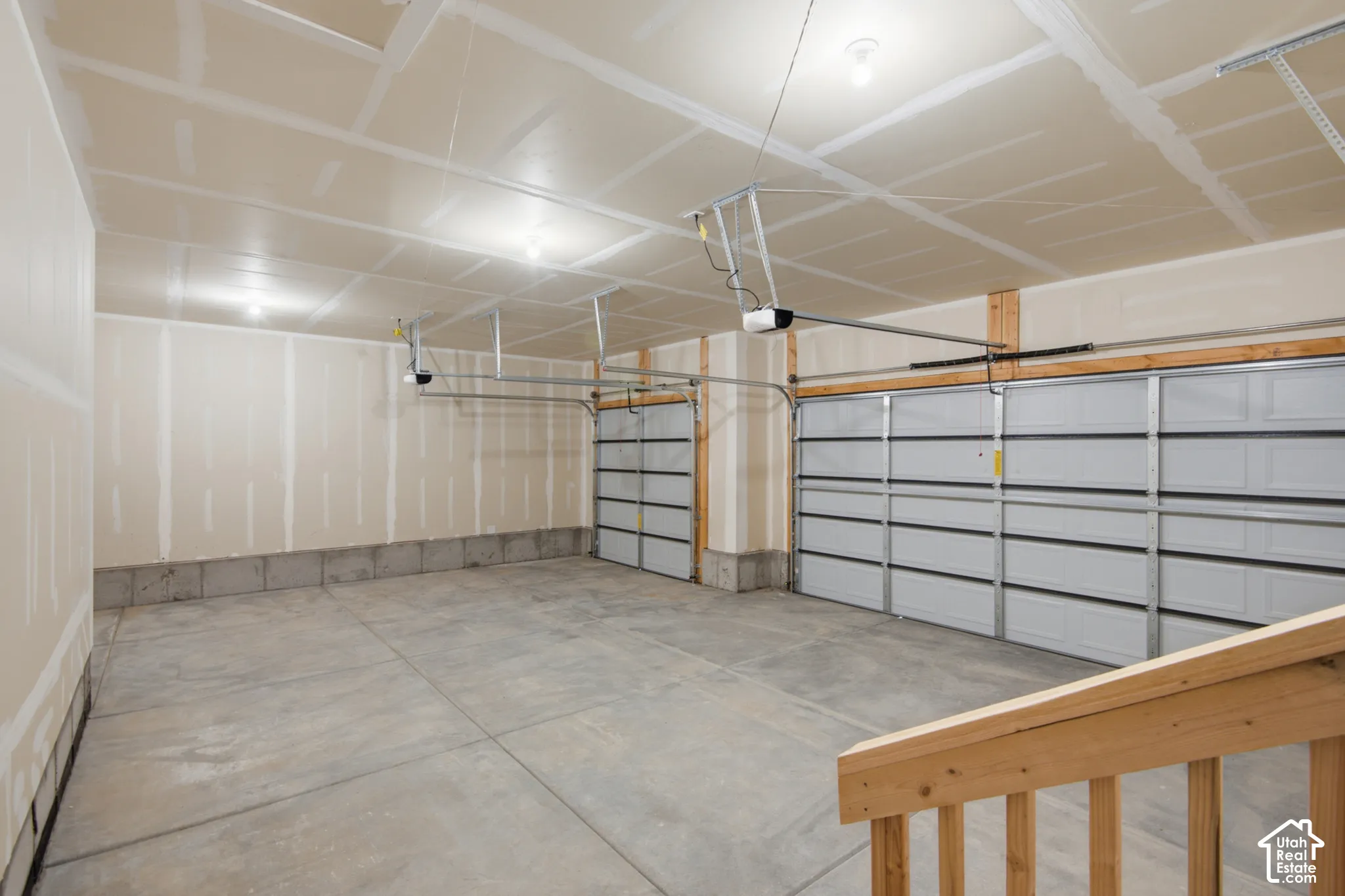 Attached three-car garage featuring drywall finish, concrete flooring, automatic openers, and wooden handrail