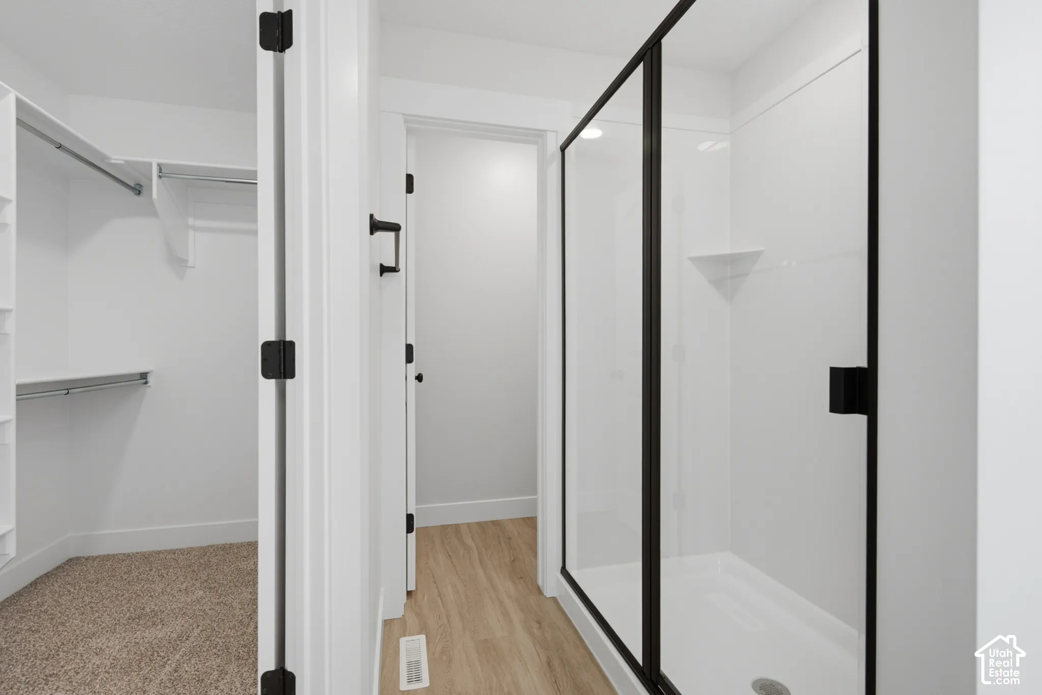 Walk-in closet with built-in shelving, shower enclosure featuring matte black framing and hardware, and wood-finish flooring