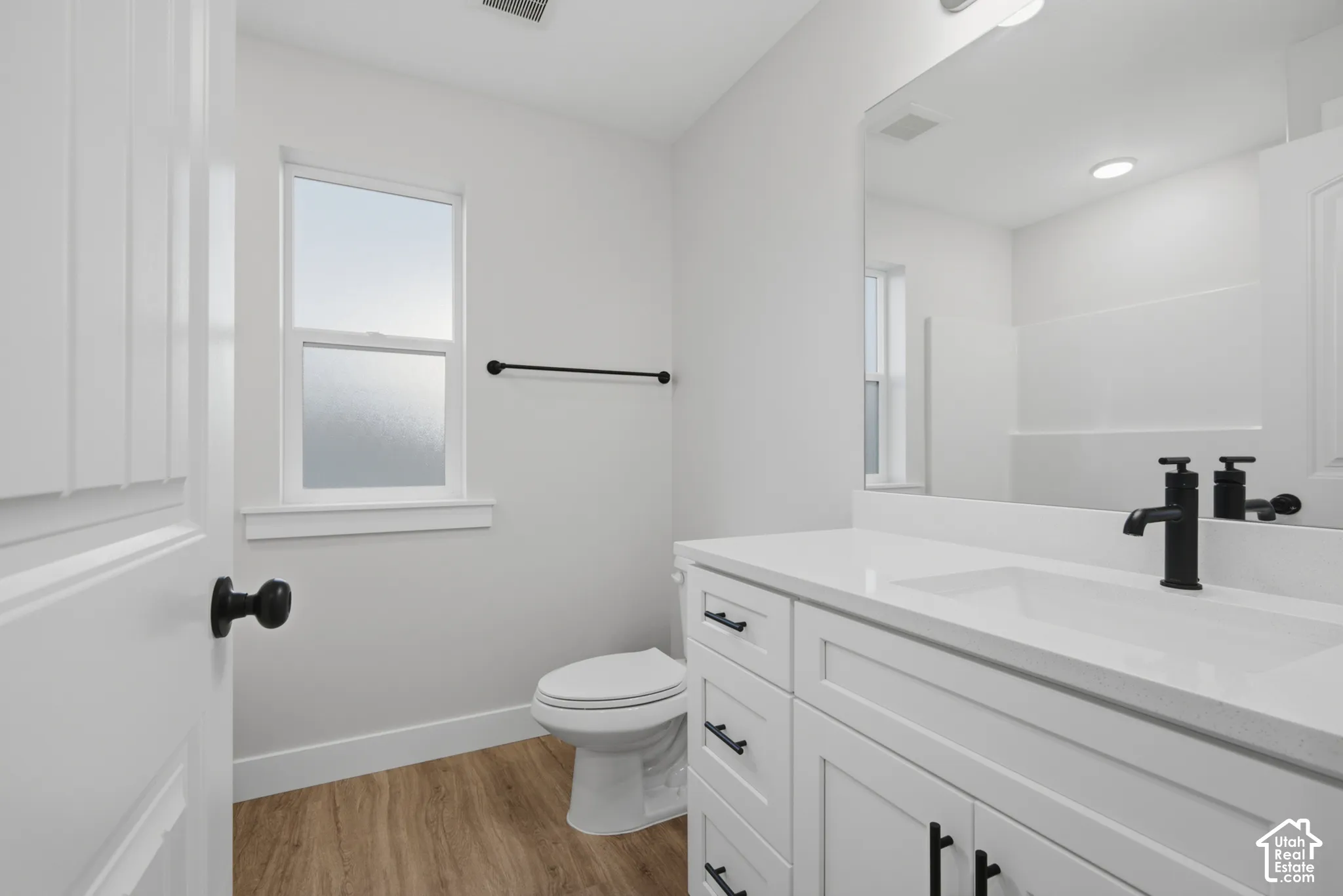 Bathroom featuring a white vanity with a composite countertop, matte black hardware, wood-finish flooring, a rectangular sink, and a large wall-mounted mirror