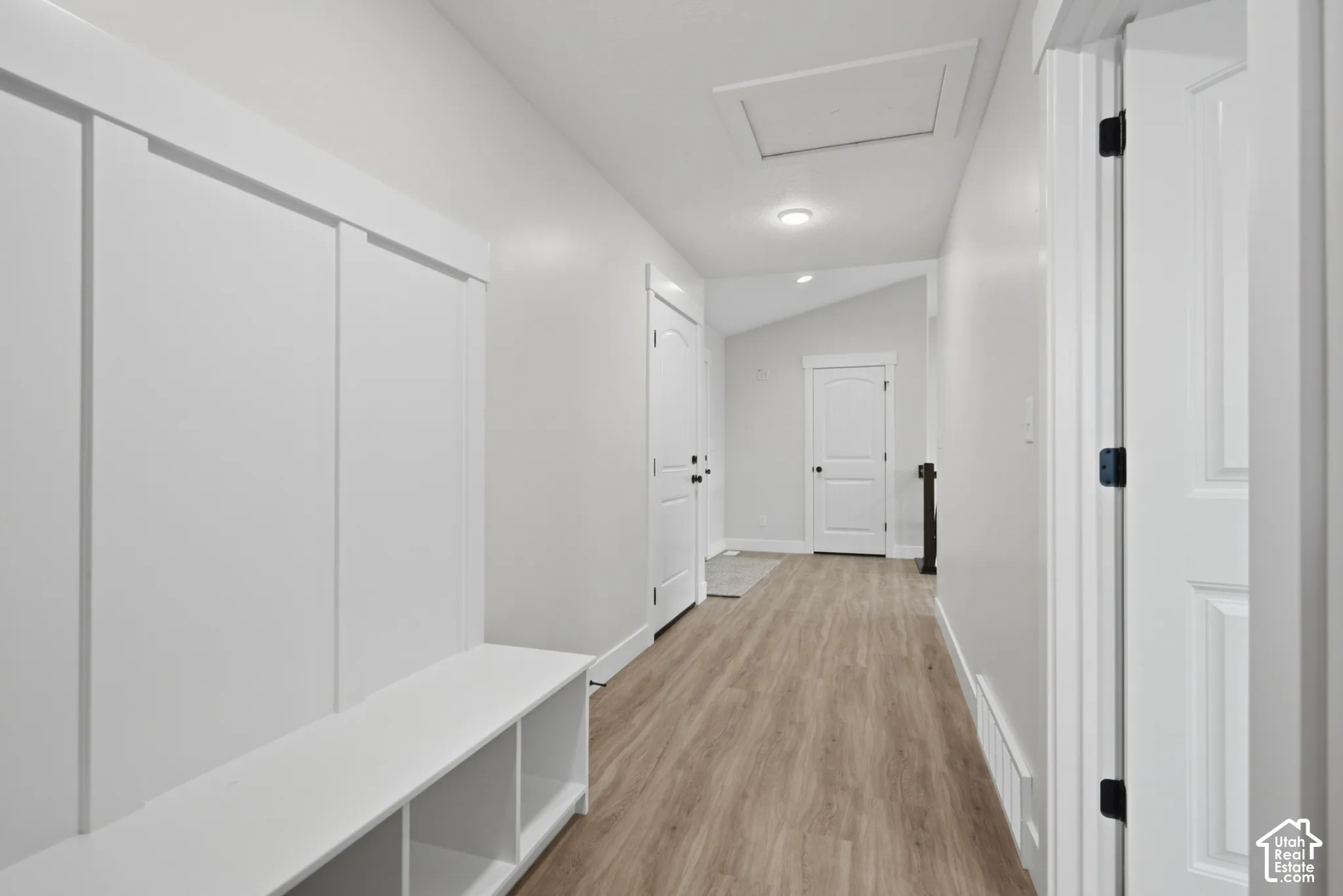 Hallway featuring wood-finish flooring, white board-and-batten wainscoting, built-in cubby storage, arched-top interior doors, and vaulted ceilings