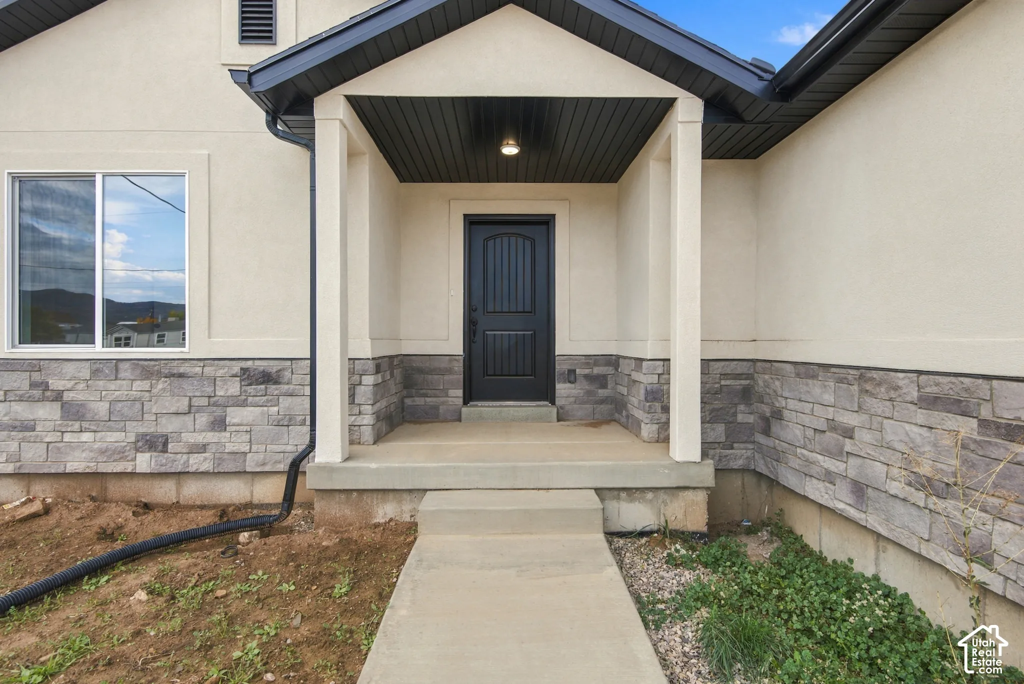 Exterior entry featuring a covered porch, stone veneer facade, stucco siding, and a dark-finished arched panel front door